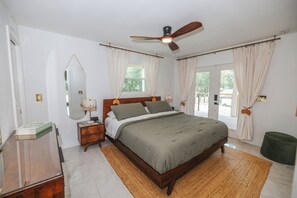 A bedroom with a bed, a ceiling fan, a nightstand, a mirror, and a window with curtains. - Boho Luxury Retreat near Winter Garden & Disney - Game Room & Statement Kitchen (Ocoee)