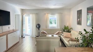 A modern living room with a sofa, a coffee table, a TV, and a fan. - Velden Pool Apartment - Large apartment with a private pool (Velden am Wörthersee)