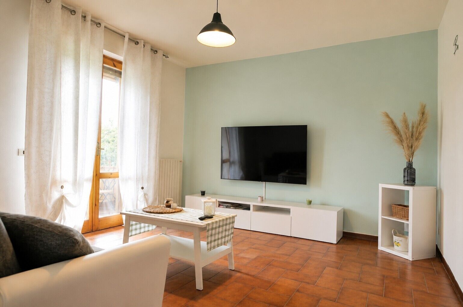 A living room with a flat-screen TV, a white sofa, a coffee table, and a TV stand with shelves.