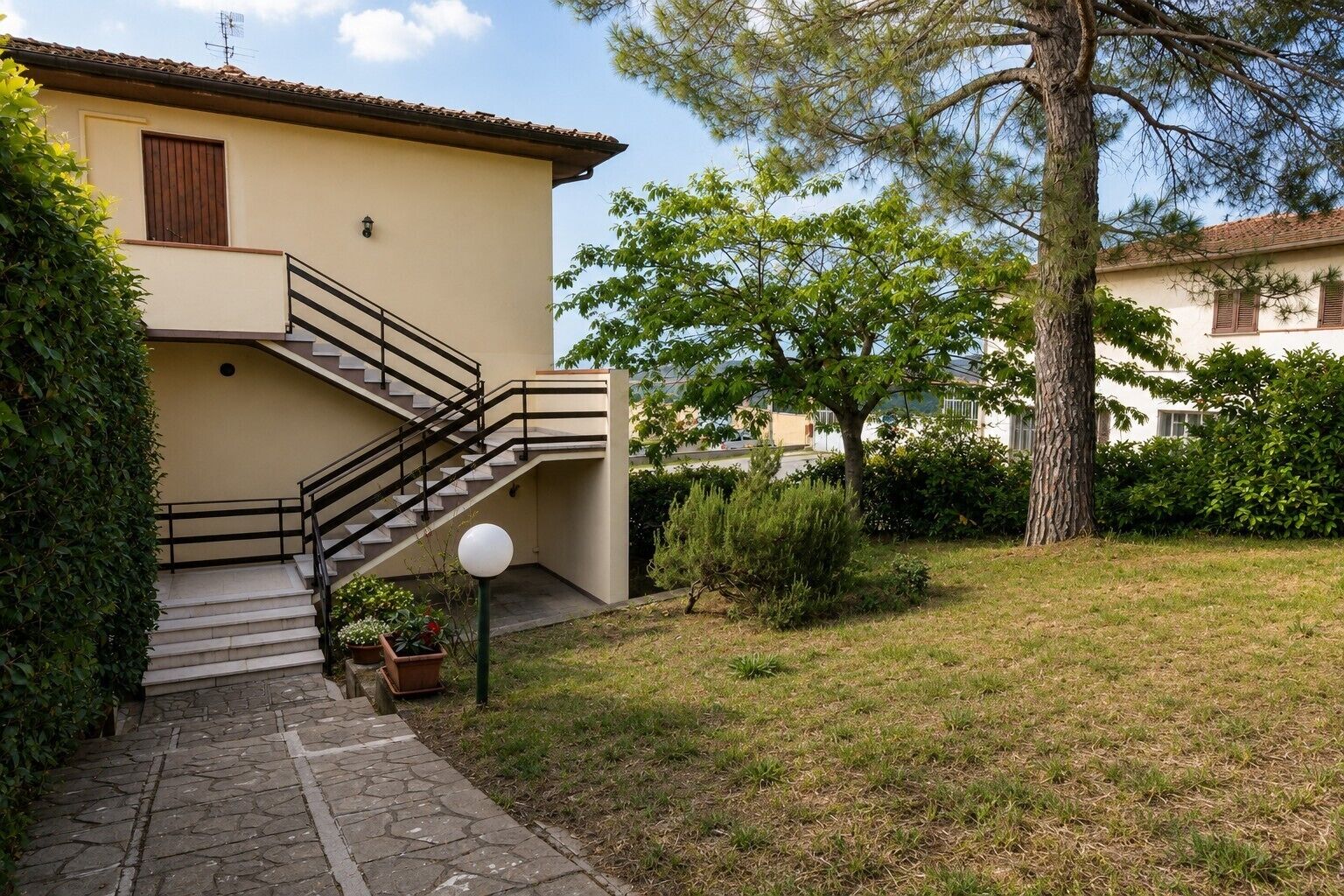 Ein Haus mit einer Treppe, die zu einer Tür führt, umgeben von einem Garten mit Gras und Bäumen.
