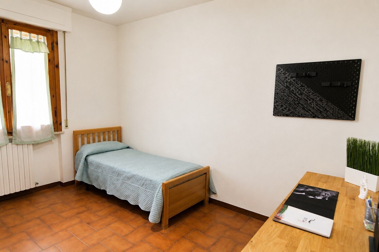 A small room with a single bed, a wooden desk, a radiator, and a window with curtains.