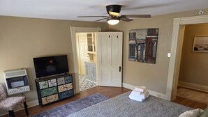 Een slaapkamer met een bed, een televisie, een dressoir, een stoel en een deur die naar een andere kamer leidt.