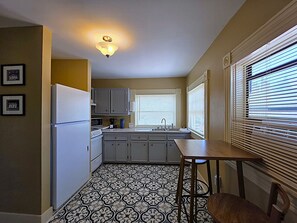 A compact kitchen with a refrigerator, sink, and window blinds.