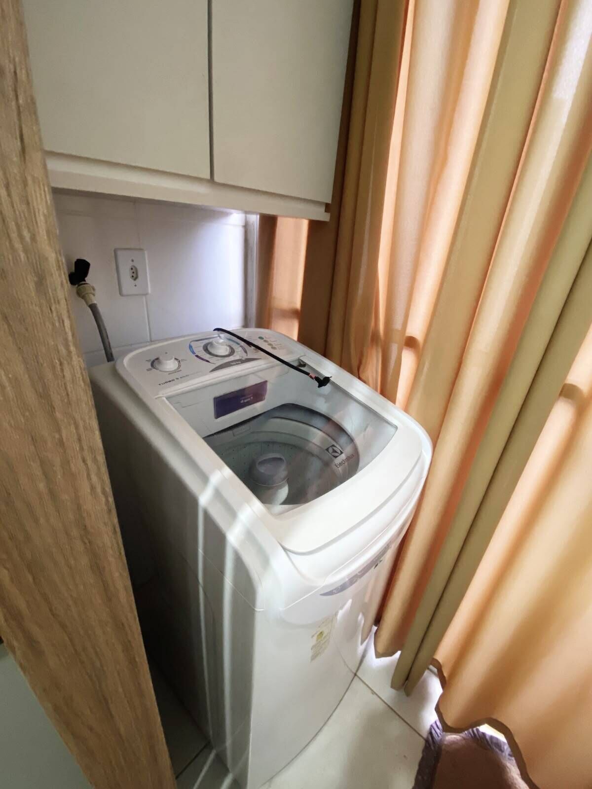 Une machine à laver compacte dans une petite pièce avec une fenêtre et des rideaux.