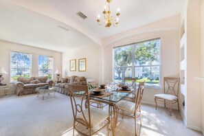 A spacious living room with a glass-top dining table, wicker chairs, and a large window offering a view of the outdoors. - 🌴NEW listing, LOW PRICE 7 bed house with pool & jacuzzi close to Disney,Epic (Kissimmee)