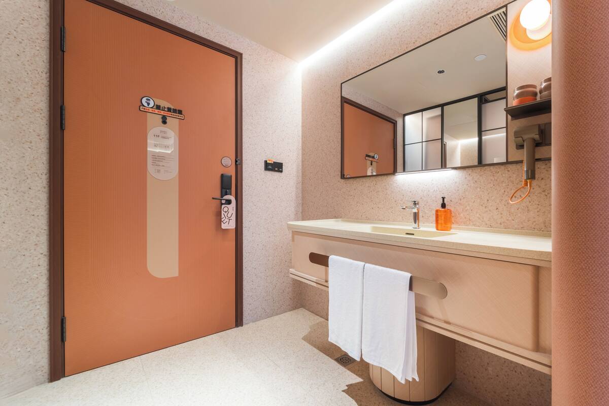 Un baño con puerta de madera, un lavabo con espejo y una toalla colgada en la pared.