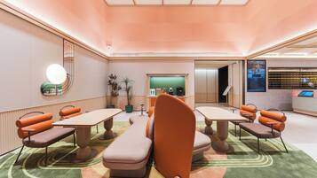 Een moderne hotellobby met een receptiebalie, een zithoek en een groene wand met een digitaal scherm.