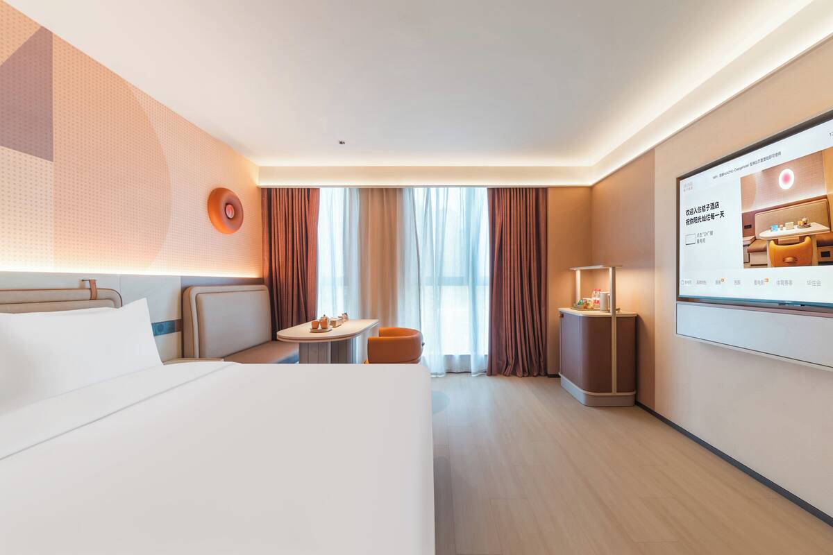 Habitación de hotel con cama, una pequeña mesa con sillas, televisión y ventana con cortinas.