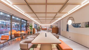 A modern conference room with a long table, comfortable seating, large windows, and a view of the outdoors.