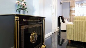 Une pièce comprenant un buffet noir et doré, un fauteuil blanc et un vase de fleurs placé sur un mur.