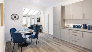 Una cucina moderna con mobili grigi, un'area pranzo con sedie blu e un grande orologio a parete.