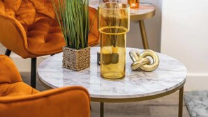 Un tavolo rotondo con un contenitore in vetro, un cesto intrecciato con piante verdi e un elemento decorativo dorato.