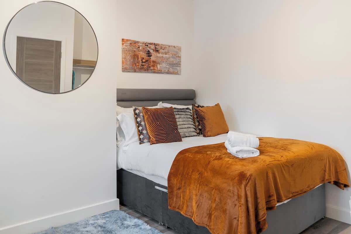 A bedroom with a bed, a round mirror, a painting, and a gray headboard.
