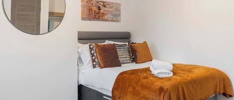 A bedroom with a bed, a round mirror, a painting, and a gray headboard.