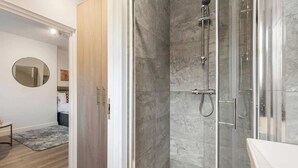 A modern bathroom with a glass shower enclosure, a round mirror, and a wooden floor. - Beautiful-Cosy-King Bed-Studio perfect for couples (Greater London)