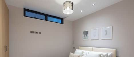 Un dormitorio con cama, mesita de noche, lámpara de pared y una ventana pequeña.