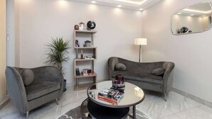 Ein modernes Wohnzimmer mit zwei grauen Sofas, einem runden Couchtisch mit Büchern, einer Stehlampe und einem Bücherregal.