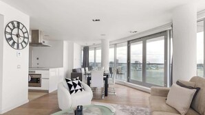 A modern apartment with a dining area, kitchen, and large windows offering a city view. - Exclusive London Penthouse with River Views (Greater London)