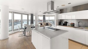 A modern kitchen with a large island, white cabinetry, and a view of the city. - Exclusive London Penthouse with River Views (Greater London)