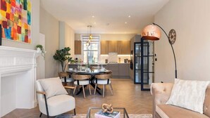 Een moderne woonkamer met een open haard, een eethoek en een keuken op de achtergrond.