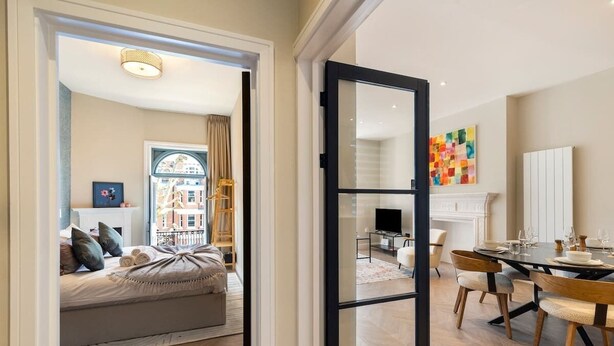 Een modern interieur met een eethoek, een bank met kussens, een open haard en een groot raam.