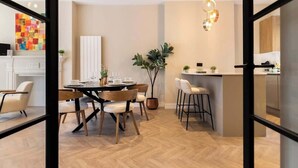 Een moderne eetruimte met een ronde tafel, stoelen, een potplant en een hanglamp.