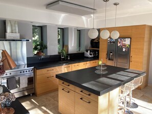 A modern kitchen with a central island, stainless steel appliances, wooden cabinets, and a large window. - Villa Pesquier - A Getaway in the Heart of the Vineyards (Gigondas)