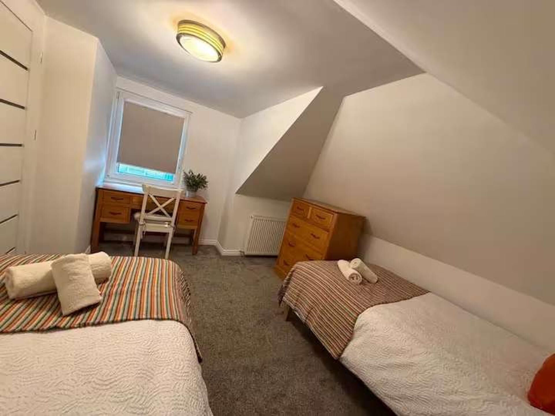 A bedroom with two beds, a desk, a chair, and a radiator.