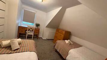A bedroom with two beds, a desk, a chair, and a radiator.