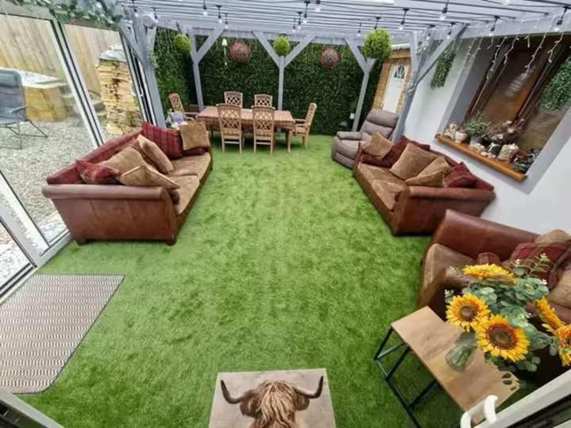 A patio area with artificial grass, a wooden table with chairs, and a sofa.