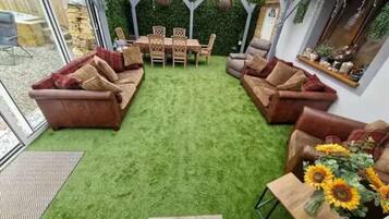 A patio area with artificial grass, a wooden table with chairs, and a sofa.