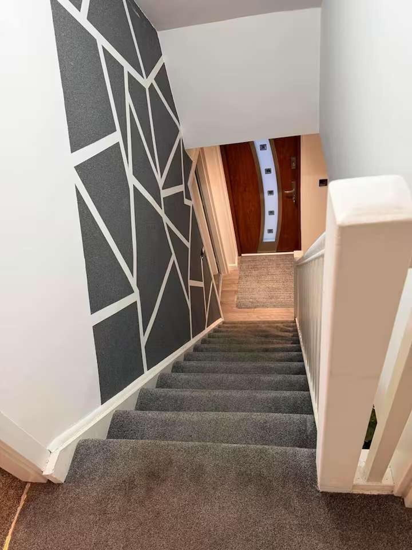 En trappe med geometrisk vægdesign, tæppede trin og en trædør for oven.