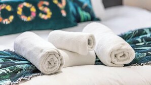 Una cama con toallas blancas enrolladas y una almohada color aguamarina con bordado floral.