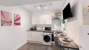 Cocina compacta con lavadora, microondas y comedor con mesa para dos.