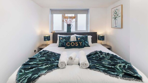 Un dormitorio con una cama, dos mesitas de noche, un ventanal y una obra de arte en la pared.