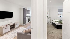 Un appartement moderne doté d’un téléviseur à écran plat, d’une kitchenette, d’une chambre avec un lit et une fenêtre, ainsi que d’un espace de vie comprenant un canapé et une table basse.