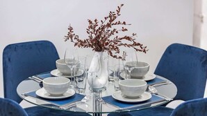 Une table ronde en verre, surmontée de bols blancs et de verres transparents, entourée de chaises bleues.
