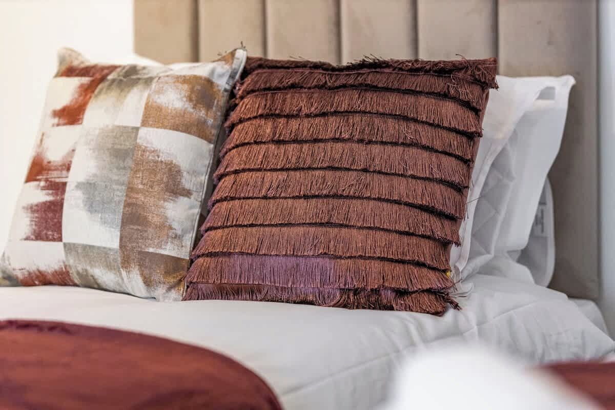 A bed with two pillows, one with a checkered pattern and the other with a fringe design.