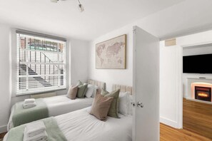 Ein Schlafzimmer mit zwei Betten, einem Kamin, einem Fernseher und einem Fenster mit Jalousien.