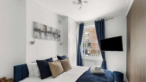 Ein Schlafzimmer mit Bett, Flachbildfernseher, Fenster mit Vorhängen und Blick auf die Stadt.