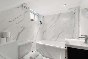 Ein modernes Badezimmer mit Marmorwänden, einer Badewanne, einer Dusche und einem Waschbecken.