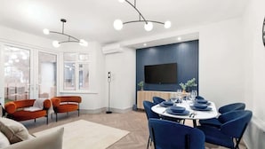Ein modernes Wohnzimmer mit Essbereich, ausgestattet mit einem großen Flachbildfernseher, einer Couch und einem Esstisch mit blauen Stühlen.