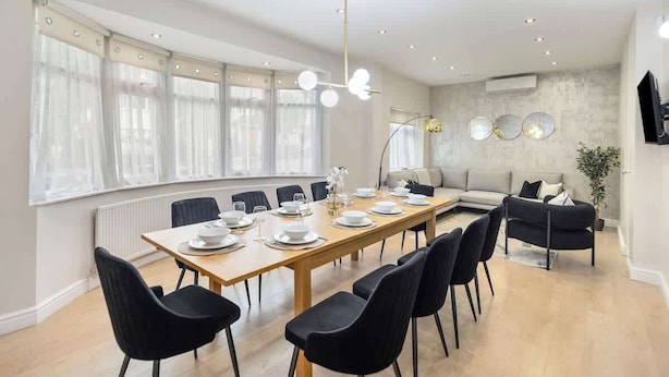 Ein modernes Esszimmer mit einem langen Tisch, schwarzen Stühlen, einer Couch und einer Deckenleuchte.