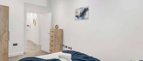 Un dormitorio con cama, cómoda, puerta y pared con un cuadro.