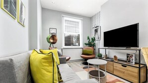 Ein modernes Wohnzimmer mit einem grauen Sofa, einem runden Couchtisch, einem Fernseher und einer Heizung.