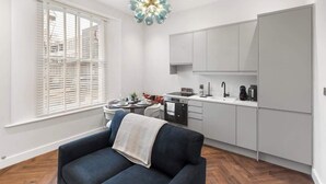 Eine moderne Küche mit weißen Schränken, einem Esstisch mit Stühlen und einem blauen Sofa mit Decke.