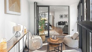 A modern living room with a sofa, a coffee table, and a dining area in the background. - Stylish Central London Flat Steps from the Tube (Greater London)