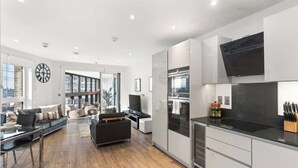 A modern kitchen with a dining area, large windows, and a flat-screen TV mounted above the counter. - Stylish Central London Flat Steps from the Tube (Greater London)