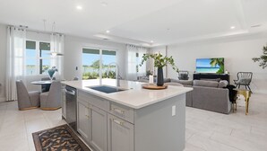 Een moderne keuken met een groot schiereiland, een eethoek met stoelen, een bank en een televisie.