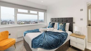 Un dormitorio moderno con una cama grande, vista a la ciudad, una silla y una mesita de noche.